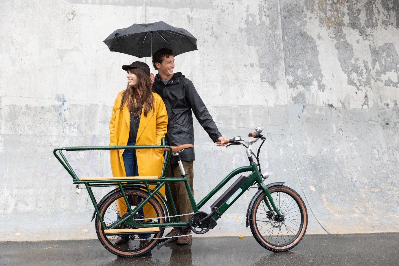 Un couple sous un parapluie qui tient un vélo électrique cargo